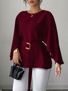 Wine red belted batwing sleeve blouse with gold buckle at waist, draped cuffs