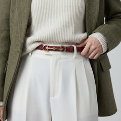Red leather belt with gold-tone double ring buckle, worn at waist with white pants.