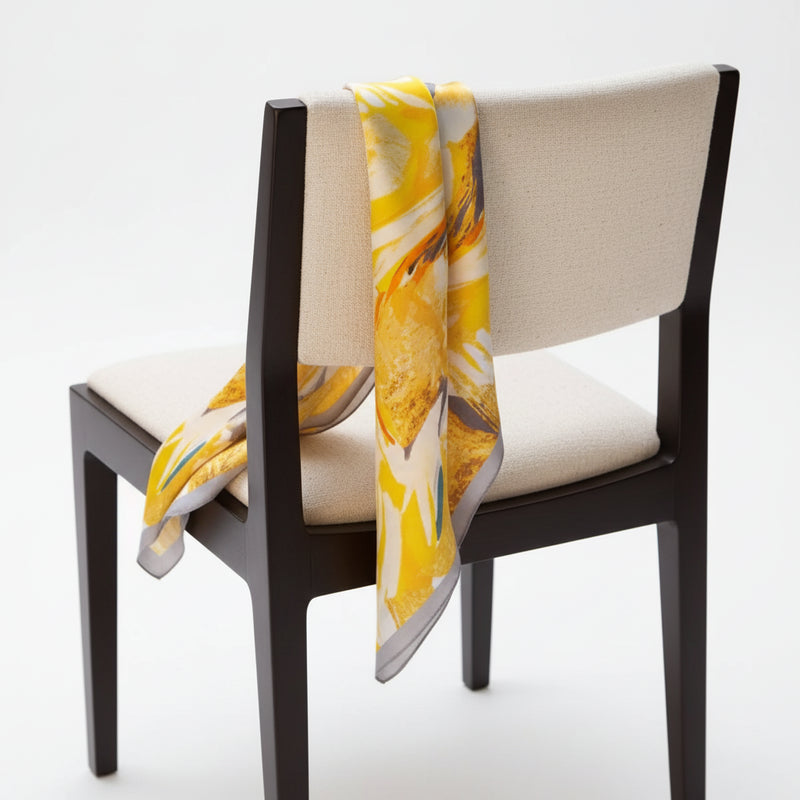 Silk square scarf draped on chair, yellow and white floral print with gray trim