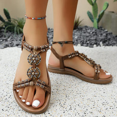 Tan open-toe flat sandals with beaded braided ankle strap and flower medallion ornament