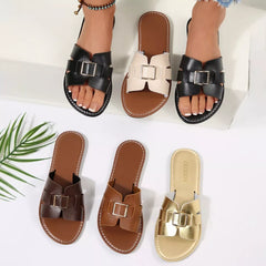 Black open-toe flat slide sandals with square buckle straps and stitched trim.
