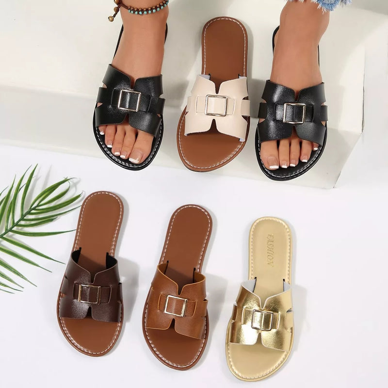 Black open-toe flat slide sandals with square buckle straps and stitched trim.