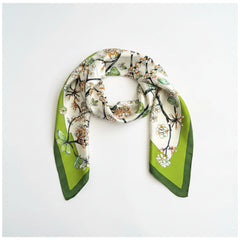 Silk scarf worn as a loop, floral branch print on light base with green edges