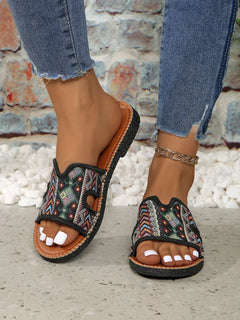 Open-toe flat sandals with black patterned straps and brown outsole, close-up