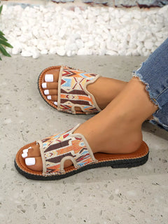 Open-toe flat sandals with tan patterned straps and brown outsole on foot