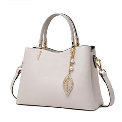 White leather top-handle handbag with crossbody strap and leaf charm on center