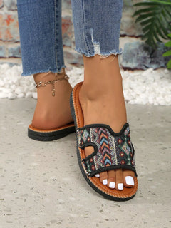 Open-toe flat sandals with dark multicolor patterned straps, brown outsole, and toe cutouts