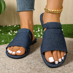 Blue open toe flat sandals with wide denim straps and dark rubber sole